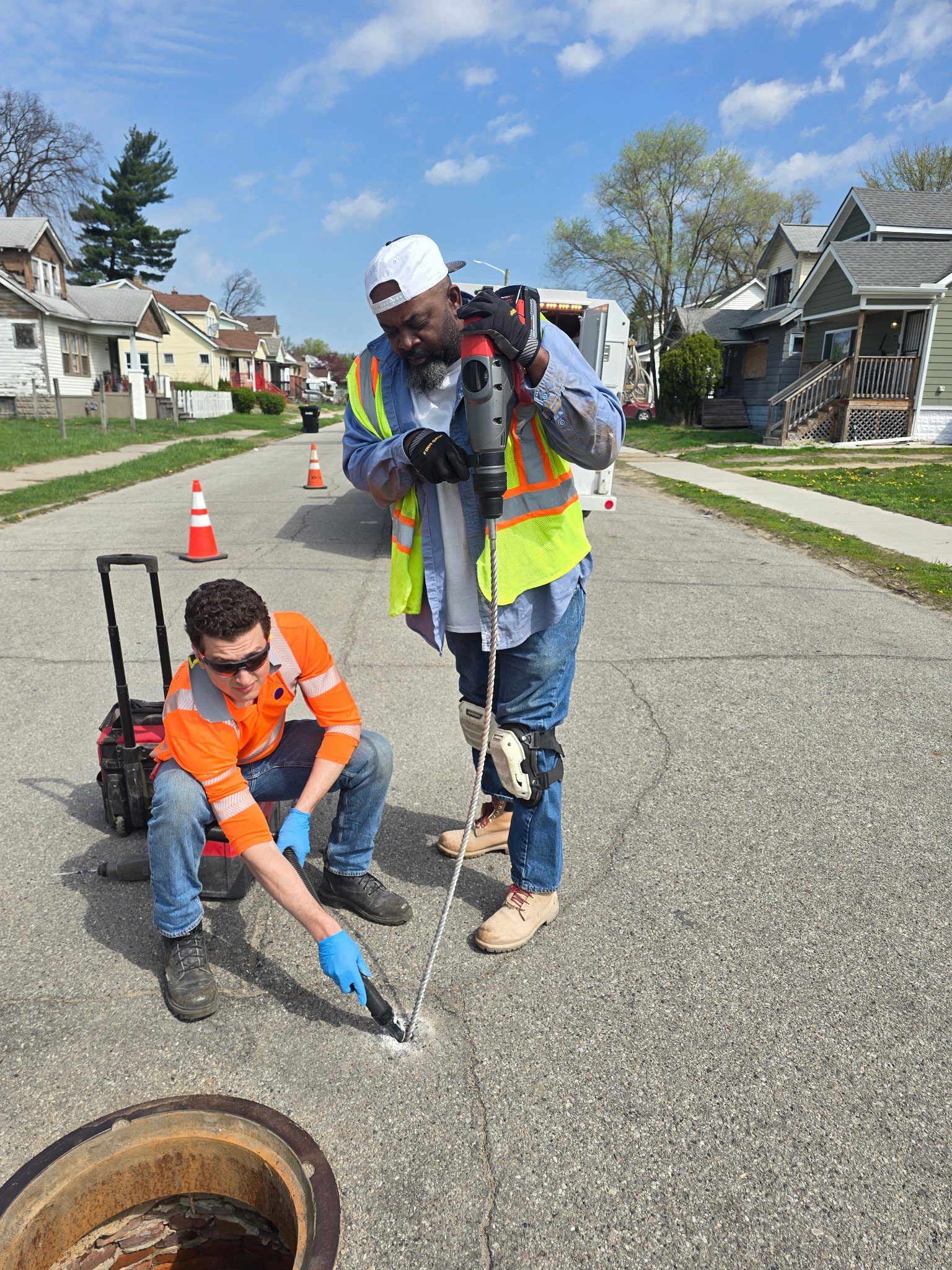 Two road workers drilling asphalt near manhole